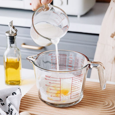 Tazza di misurazione di vetro bollente della cucina con i grafici rossi microonda e forno
