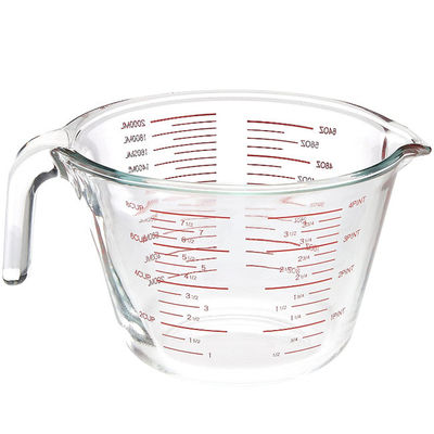 Tazza di misurazione di vetro bollente della cucina con i grafici rossi microonda e forno