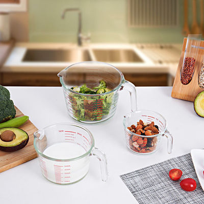 Tazza di misurazione di vetro bollente della cucina con i grafici rossi microonda e forno