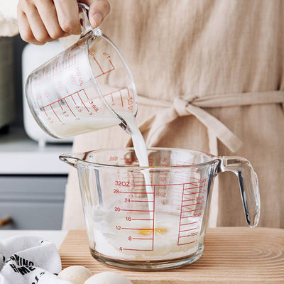Tazza di misurazione di vetro bollente della cucina con i grafici rossi microonda e forno